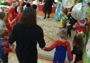 Dzieci z grupy Stokrotki wraz z nauczycielkami tańczą w kółeczku.