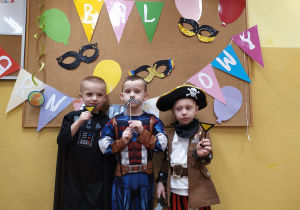 Trzech chłopców w strojach ulubionych postaci z bajek pozują do zdjęcia na tle dekoracji karnawałowej.