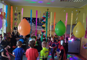 Dzieci tańczą w kole do ulubionych dyskotekowych piosenek w Sali udekorowanej girlandami i balonami.