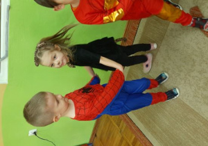 Chłopiec przebrany za Spider-Mana tańczy z dziewczynką przebraną za czarnego kotka.
