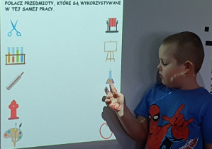 Chłopiec na tablicy interaktywnej stara się połączyć przedmioty, które wykorzystuje się podczas tej samej pracy.