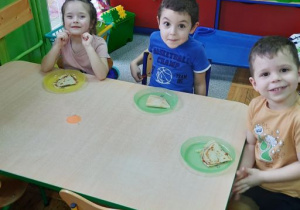 Dzieci przy stoliku zajadają się przygotowanymi przez siebie naleśnikami.