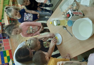 Z niewielką pomocą nauczyciela dziewczynka rozbija jajko do plastykowego talerzyka.