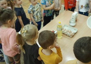 Dzieci stoją wokół stolika, na którym leżą produkty do zrobienia ciasta na naleśniki.