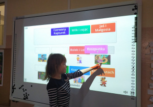 Dziewczynka wskazuje na tablicy interaktywnej rozwiązanie quizu dotyczącego ulubionych bajek.