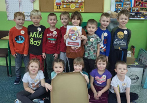 Dzieci z grupy Motylki pozują do wspólnego zdjęcia. W tle napis Dzień Pizzy. Z przodu trzymają karton z przygotowaną papierową pizzą zgodnie z przepisem.
