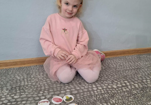 Dziewczynka w opasce z kokardką siedzi przed obrazkami ułożonymi według kodu i przedstawiającymi składniki na pizzę.