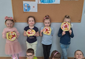 Dzieci trzymają w re ku papierowe pizzę, które wcześniej wykonały.