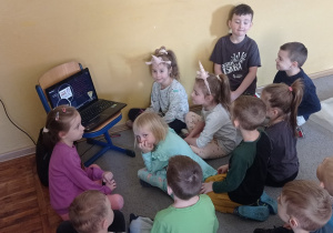 Dwanaścioro dzieci jest zgromadzonych przed laptopem, na którym jest wyświetlany film dydaktyczny pt.:” Ciekawostki o pizzy”.