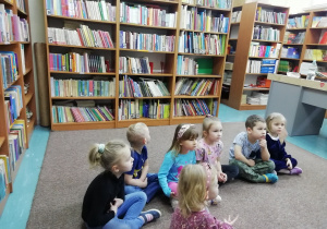 Siódemka dzieci siedzi na dywanie w bibliotece.