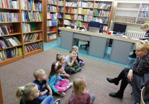 Dzieci siedzą na dywanie przed Panią z biblioteki.