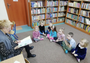 Dzieci siedzą i słuchają książki czytanej przez Panią z biblioteki.