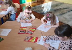 Dzieci z grupy Słoneczka siedzą przy stoliku i kolorują malowanki z pączkami.