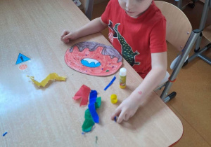 Chłopiec z grupy Liski dekoruje kuleczkami z bibuły kolorowankę donuta.