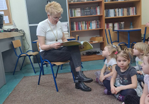 Zdjęcie przedstawia jak pani pracująca w bibliotece czyta dzieciom bajeczkę.