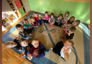 Zdjęcie grupowe dzieci siedzących na dywanie podczas gry tematycznej.
