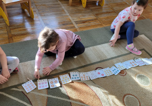 Dziewczynka siedzi na dywanie przed rozłożonymi karatami i przypina klamerkę na właściwą cyfrę