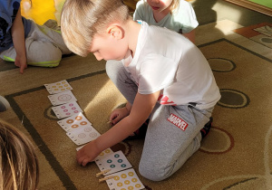 Chłopiec siedzi na dywanie przed rozłożonymi karatami i przypina klamerkę na właściwą cyfrę