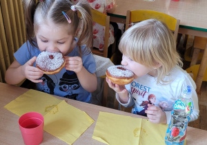Dwie dziewczynki siedzą przy stoliku i jedzą pączki