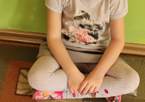 Dziewczynka siedzi na dywanie i prezentuje ułożony przez nią obrazek pączków