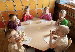 Dzieci siedzą przy stoliku i jedzą paczki.