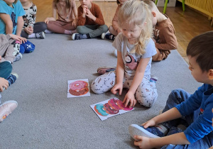 Dzieci siedzą w kole na dywanie, jedna dziewczynka układa puzzle.