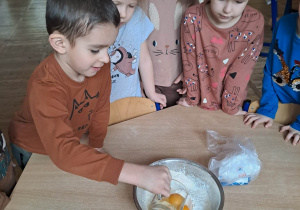 Chłopiec wlewa jajka do miski , część dzieci się przygląda.