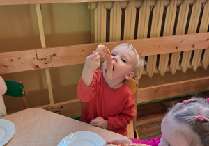 Chłopiec ochoczo zajada kawałek pizzy przy stoliczku.