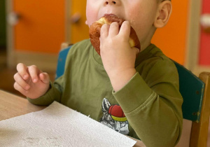 Chłopiec zajada przy stoliczku pączka.