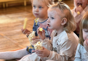 Dziewczynki zajadają popcorn i chrupki oglądając bajkę.