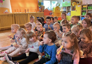 Dzieci zajadają popcorn i chrupki oglądając bajkę.