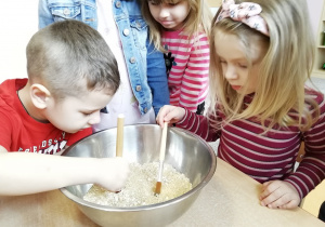 Dzieci przeganiają pędzelkami płatki owsiane i ryż znajdujący się w misce.