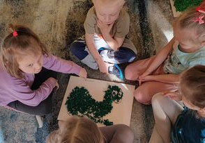 Dzieci siedzą na dywanie prezentują swojego wcześniej wyklejonego dinozaura.