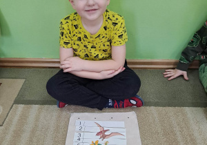 Na zdjęciu chłopczyk ułożył obrazek przedstawiający dinozaury dobrze się przy tym bawiąc.
