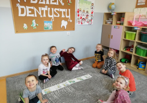 Dzieci siedzą na dywanie a między nimi leża ilustracji z historyjką obrazkową.