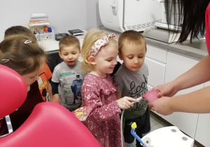 Dzieci są w gabinecie dentystycznym, a jedna z dziewczynek trzyma w ręku rurkę dentystyczną.