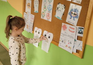 Dziewczynka z grupy Misie, stoi przy tablicy i „karmi” smutnego zęba, wylosowanym wcześniej produktem