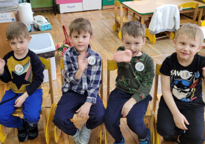 Czterech chłopców siedzi na krzesełkach jako jurorzy i machają na powitanie