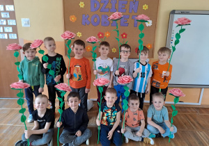 Chłopcy pozują na tle tablicy dekoracyjnej z różami, które zrobiły dla swoich mam.