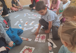Dzieci siedzą w kółeczku na dywanie i jeden z chłopców układa puzzle.