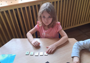 Dziewczynka siedzi przy stoliku i wykonała działanie matematyczne.