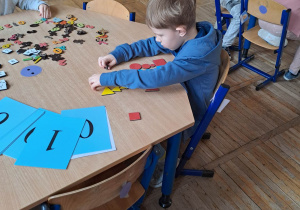 Chłopiec siedzi przy stoliku i układa obrazek z figur geometrycznych.