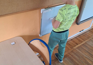 Chłopiec stoi przy tablicy magnetycznej i wykonuje działanie matematyczne.