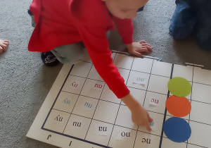 Chłopiec w czerwonej bluzie koduje sylabę „ne” na macie do kodowania.
