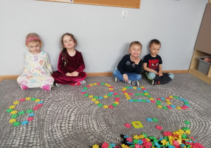 Czwórka dzieci siedzi przy ścianie, a przed każdym z nich leżą cyfry 10 ułożone z klocków.