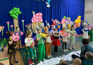 Dzieci w strojach śpiewają piosenkę z szablonami kolorowych kwiatów w rękach.