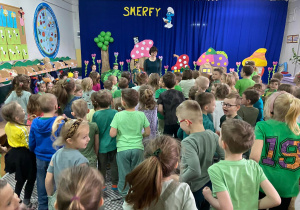 Dzieci ubrane w zielone bluzki na tle dekoracji przedstawiającej wioskę smerfów