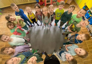 Dzieci z grupy Żabki stoją na dywanie w kolorowych skarpetkach. Ze swoich stóp utworzyły kształt serca.