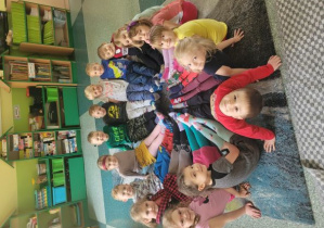 Dzieci z grupy Motylki siedzą na dywanie i prezentują swoje kolorowe skarpetki.