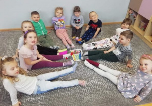 Dzieci z grupy Liski siedzą na dywanie w kolorowych skarpetkach dookoła obrazka z napisem Światowy Dzień Osób z Zespołem Downa.